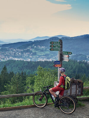 Ein Radfahrer blickt auf einer Aussichtsstelle über Bodenmais und den Bayerischen Wald.