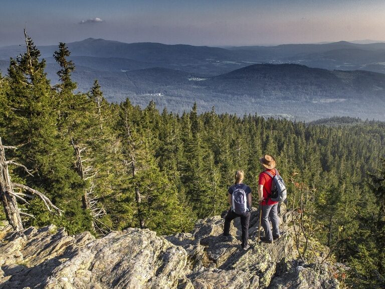 Zwei Wanderer genießen vom Falkenstein Gipfel die unvergleichliche Aussicht auf den grünen Bayerischen Wald.