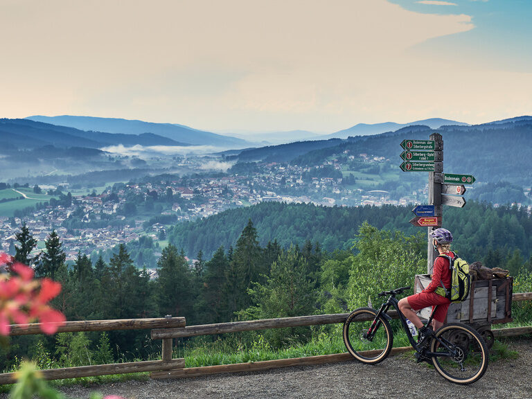 Ein Radfahrer blickt auf einer Aussichtsstelle über Bodenmais und den Bayerischen Wald.