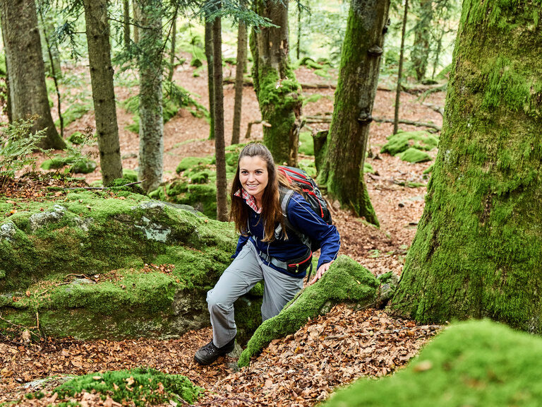 Eine Frau steigt einen Hang in einem Waldstück des Bayerischen Waldes hoch