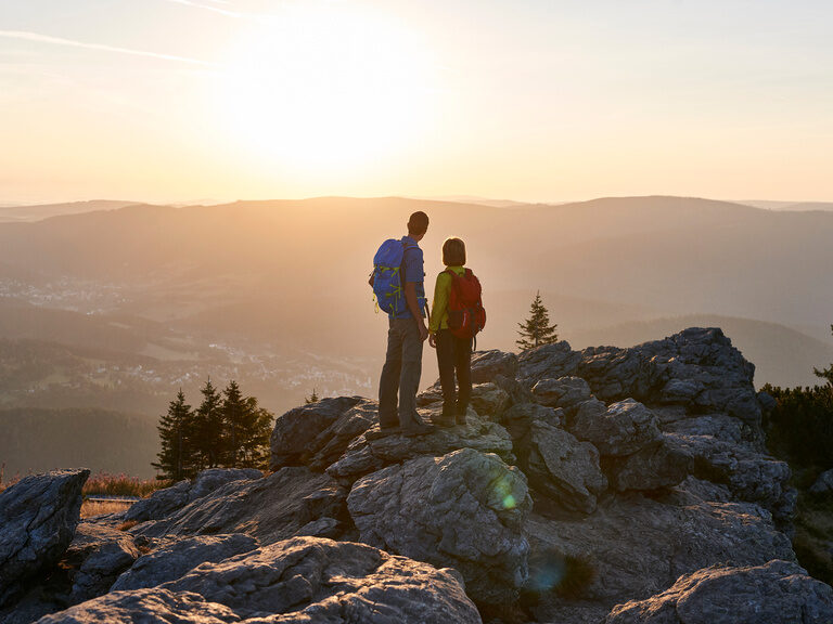 Wanderer pausieren auf einem Gipfel, während sich das Bergpanorama hinter ihnen erstreckt.